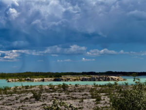 Turquoise quarry lake with limestone cliffs, forested shoreline, and dramatic cloudy sky with crepuscular rays