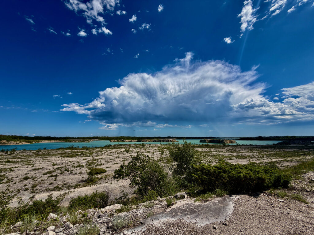 Turquoise lagoon surrounded by limestone terrain and sparse vegetation under a bright blue sky with white clouds