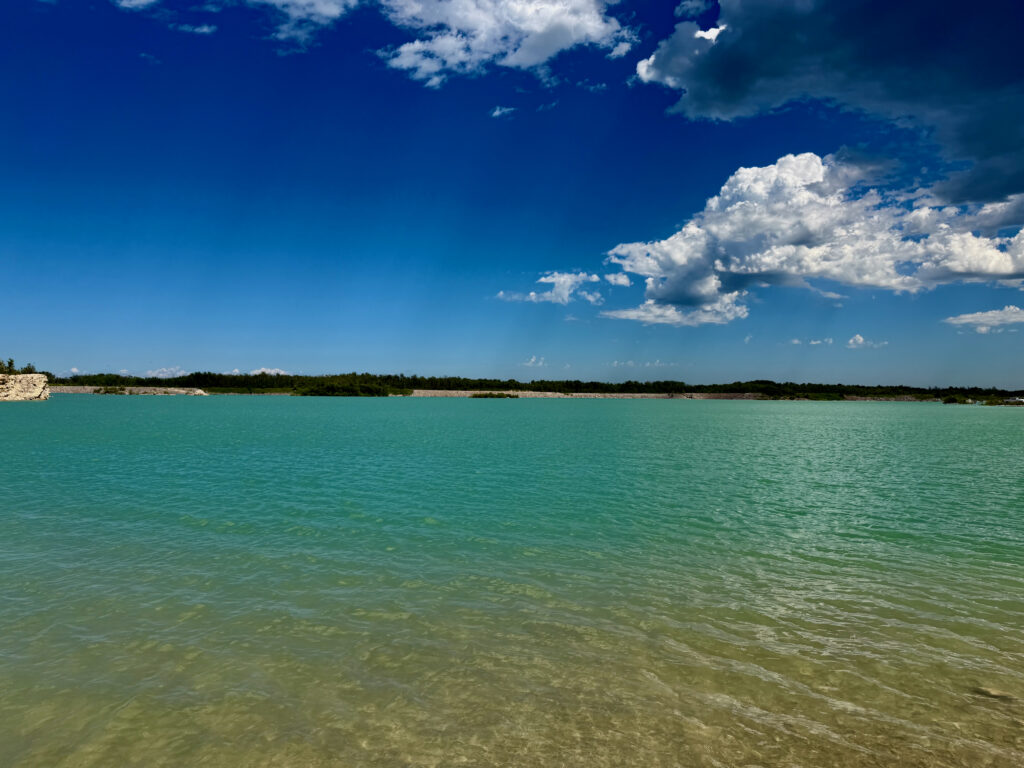 Turquoise water and sandy beach with forested shoreline under a blue sky with white clouds