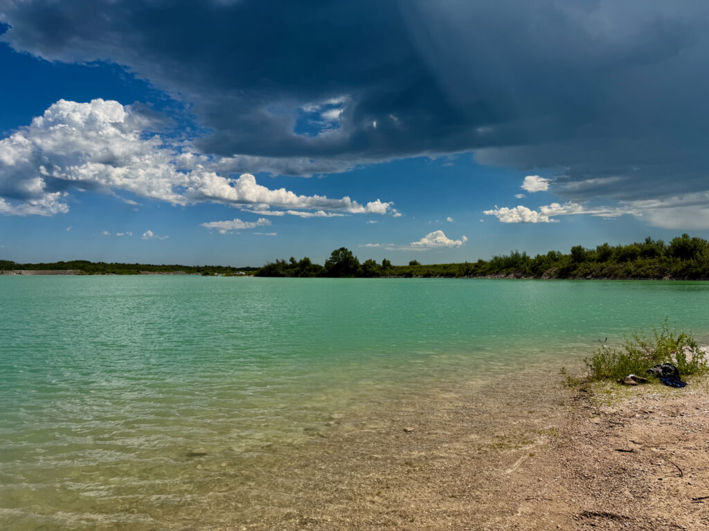 Turquoise lagoon with sandy beach, tree-lined shore, and blue sky with white clouds