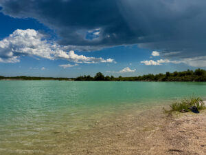 Turquoise lagoon with sandy beach, tree-lined shore, and blue sky with white clouds