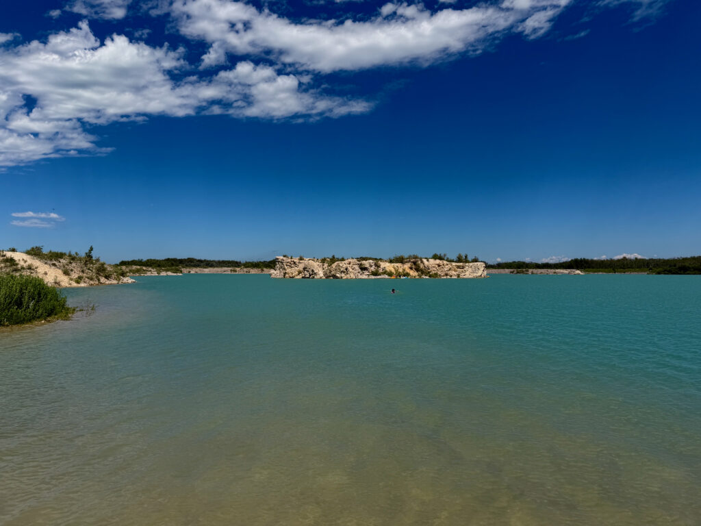 Turquoise lake with limestone cliffs, forested shoreline, and clear blue sky with white clouds