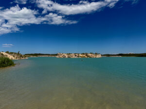 Turquoise lake with limestone cliffs, forested shoreline, and clear blue sky with white clouds
