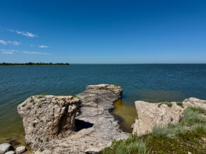 Rocky limestone formations jutting from turquoise water under clear blue sky, with forested shoreline in the distance