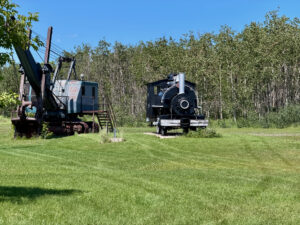 Two vintage railway locomotives displayed on grass with aspen trees in the background on a clear sunny day