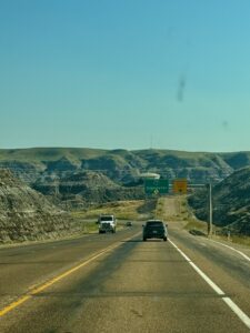 Highway approaching Drumheller with directional signs and deeply eroded badlands terrain on both sides of the road