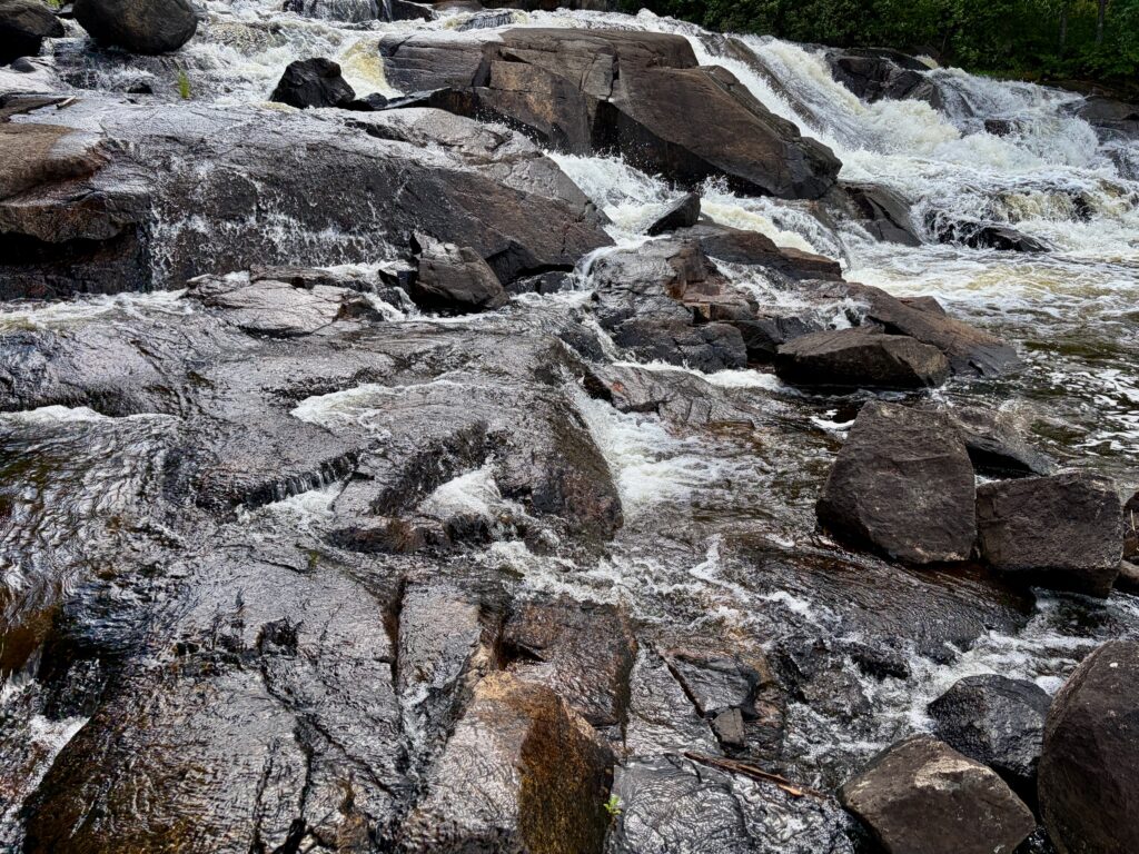 Turbulent river with whitewater cascading over dark boulders and rocky outcrops, surrounded by evergreen forest
