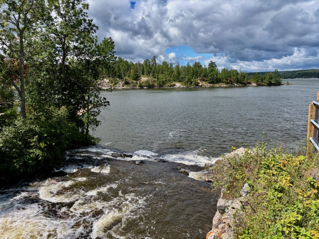 Rocky shoreline with waves washing against the shore, boreal forest and distant rocky islands under cloudy sky