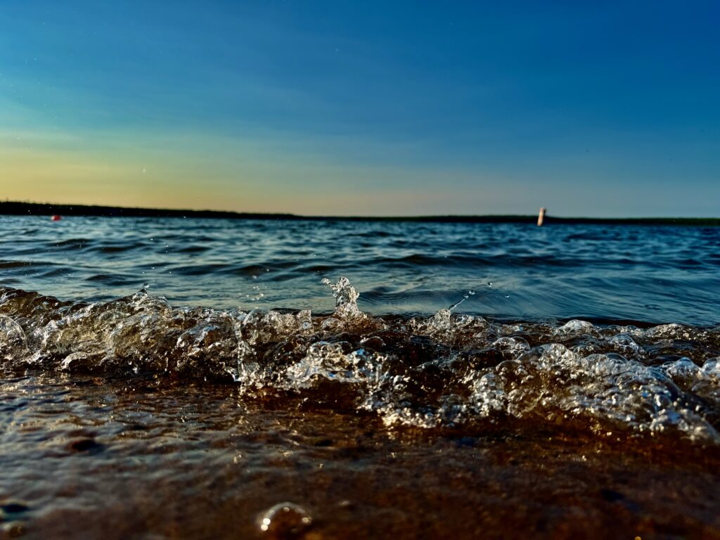 Waves breaking on a sandy beach with clear blue sky and distant sailboat on the horizon