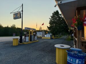 Vintage gas station with "Fuel Up Here!" sign, yellow pumps, and Nutimik Lodge building at dusk with Canadian flag