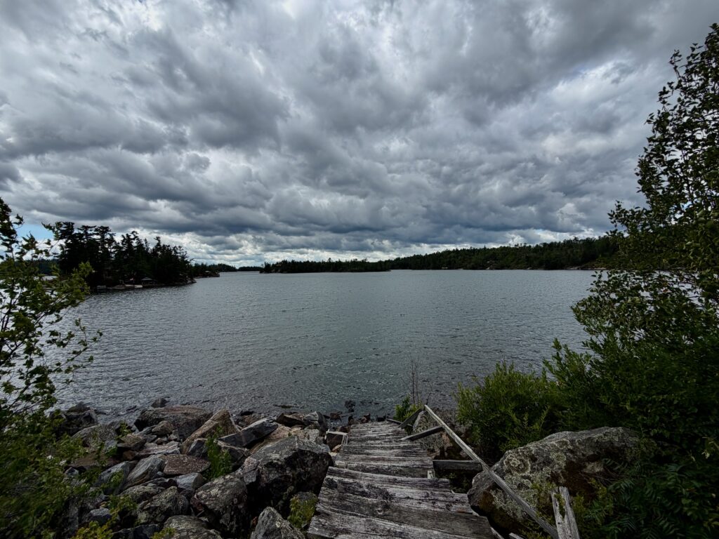 Wooden dock extending into a calm lake surrounded by boreal forest under dramatic storm clouds