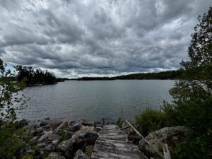 Wooden dock extending into a calm lake surrounded by boreal forest under dramatic storm clouds
