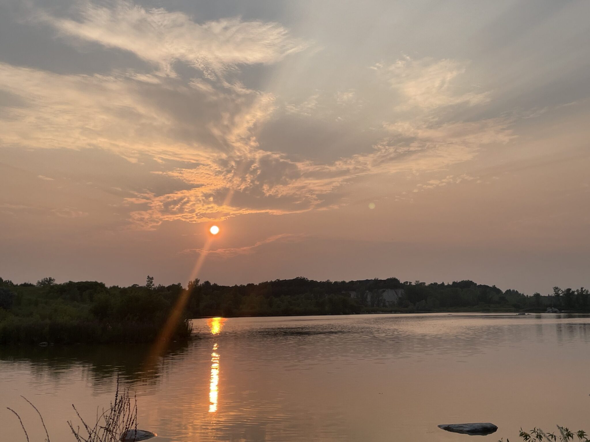 Sunset over a calm river with golden light reflecting on the water, trees lining both shores, and dramatic clouds in the sky