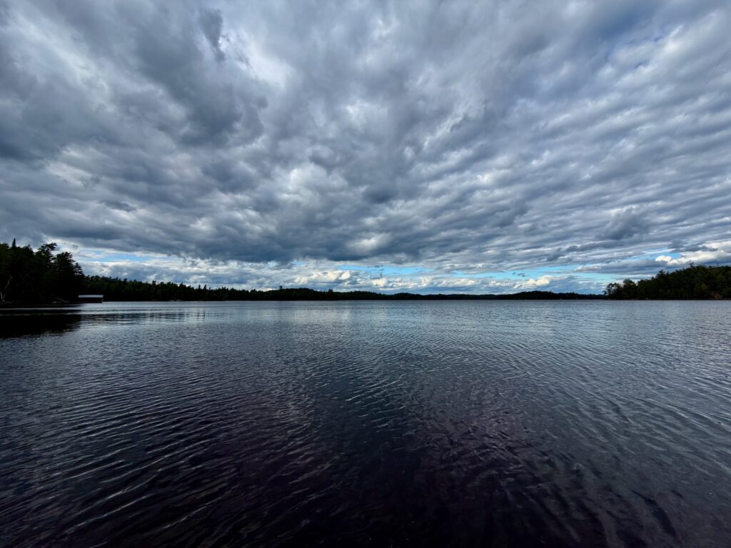 Lake with forested shoreline under dramatic cloudy sky