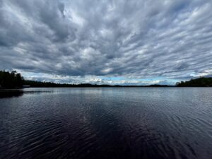 Lake with forested shoreline under dramatic cloudy sky