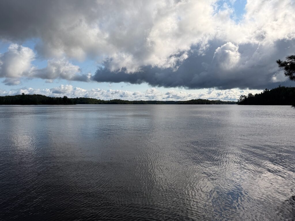 Lake surrounded by forested shoreline under a sky with white and grey clouds