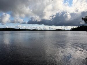 Lake surrounded by forested shoreline under a sky with white and grey clouds