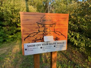 Wooden sign featuring Smokey the Bear wearing a ranger hat, with instructions to take a selfie: set phone on ledge, open camera app and set timer, then smile for Smokey