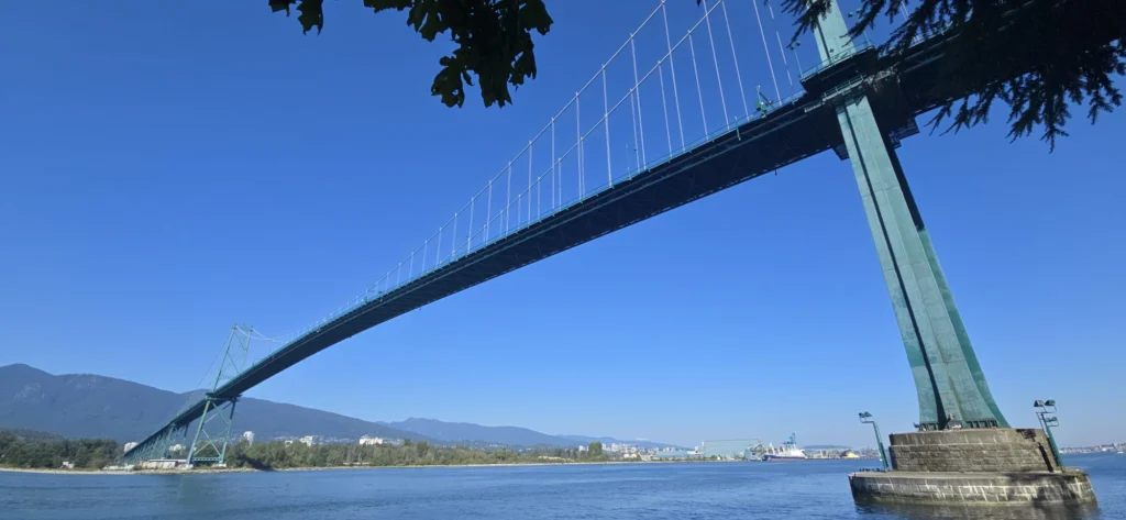 Lions Gate Bridge spanning Burrard Inlet with North Shore mountains in the background under clear blue sky