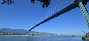 Lions Gate Bridge spanning Burrard Inlet with North Shore mountains and Vancouver skyline visible under clear blue sky