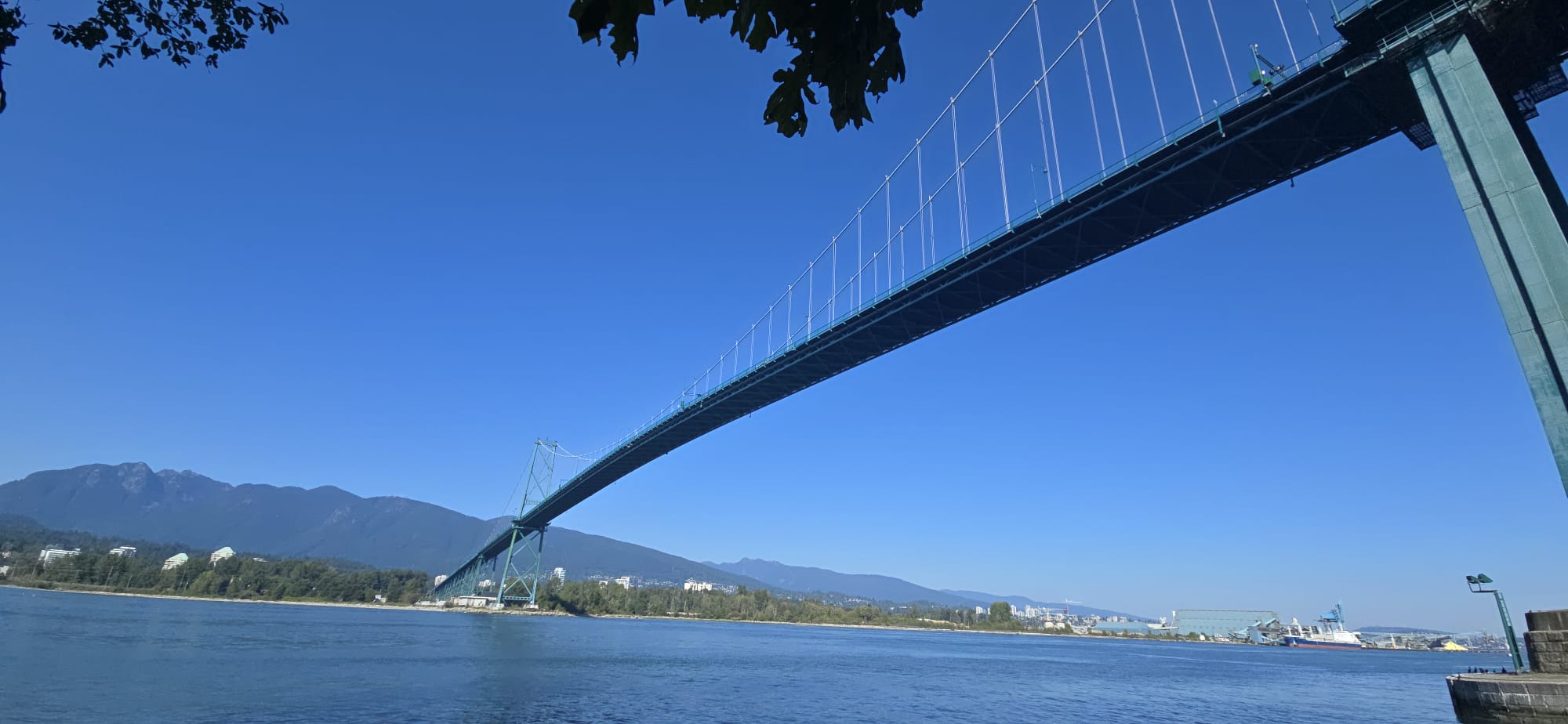 Lions Gate Bridge spanning across Burrard Inlet with North Shore mountains in the background under clear blue sky